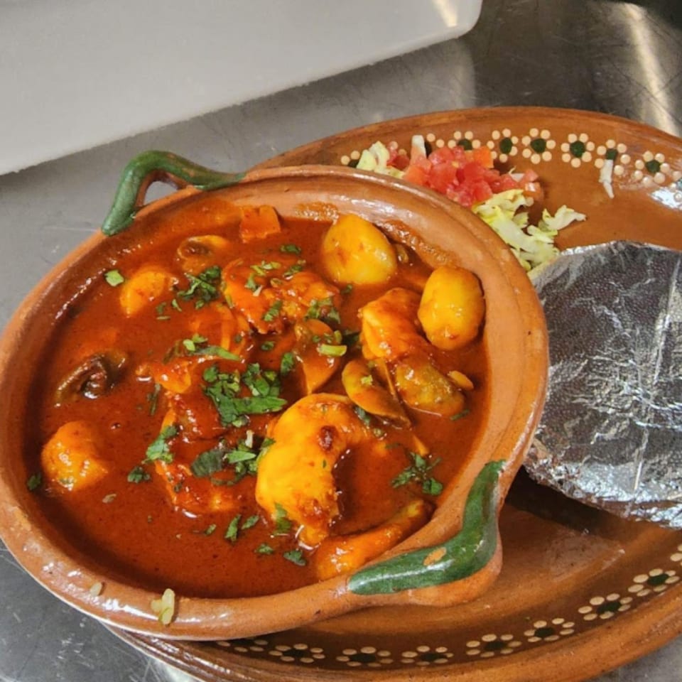 Mexican shrimp and potato stew in a clay bowl with a side of salad and tortillas.