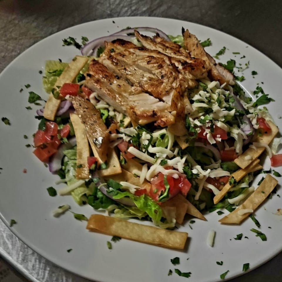 Grilled chicken salad with lettuce, tomatoes, red onions, cheese, and tortilla strips.