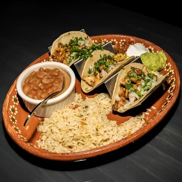 Three El Centenario WPB tacos with rice, beans, sour cream, and guacamole on a terracotta plate.