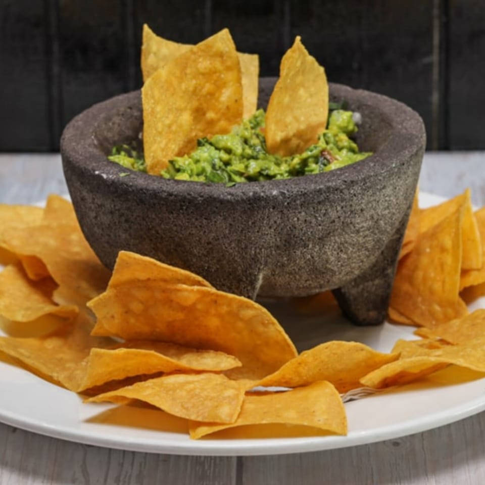 Fresh guacamole in a stone molcajete, surrounded by crispy tortilla chips on a white plate.