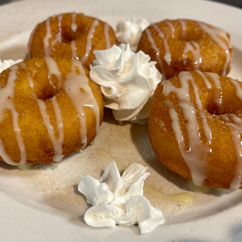 Four golden-brown Mexican donuts drizzled with white icing and garnished with whipped cream.