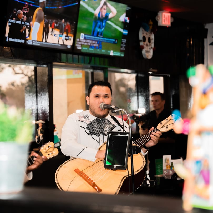 A mariachi singer in a charro suit performs with a guitar in a lively Mexican restaurant.