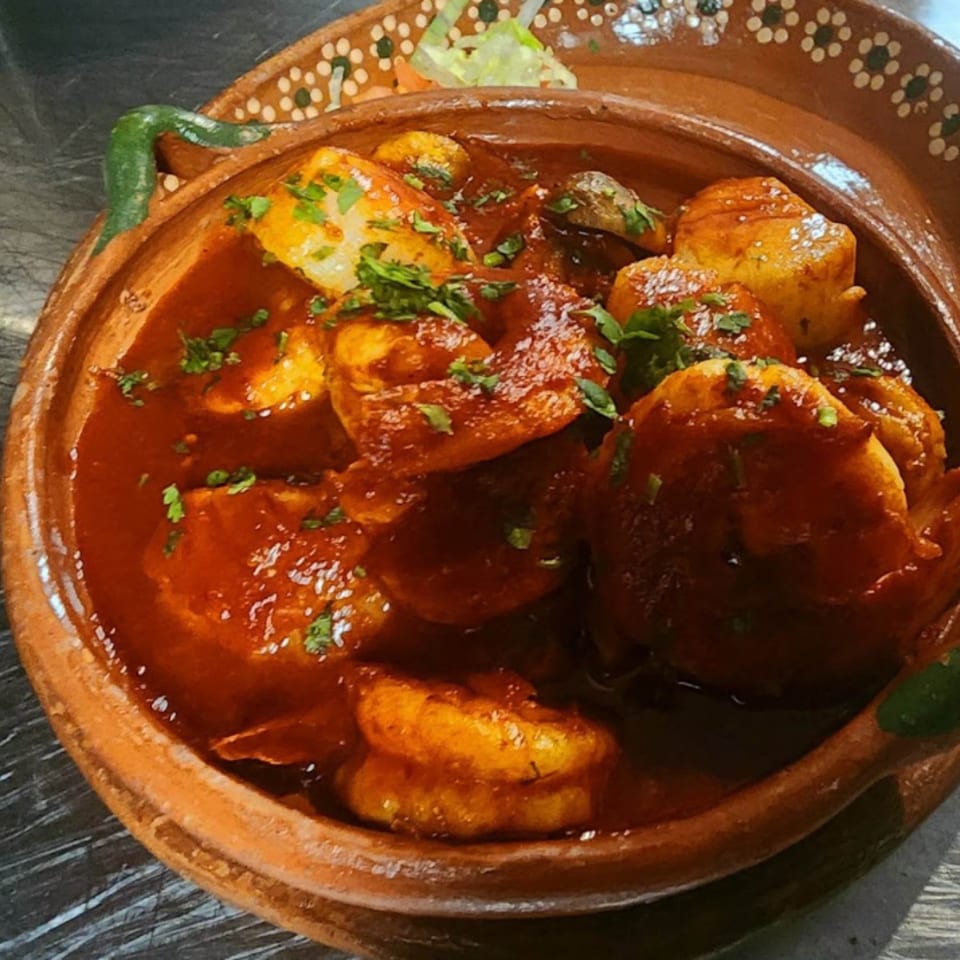 Shrimp and potatoes in a rich red sauce, garnished with cilantro, served in a traditional Mexican clay bowl.