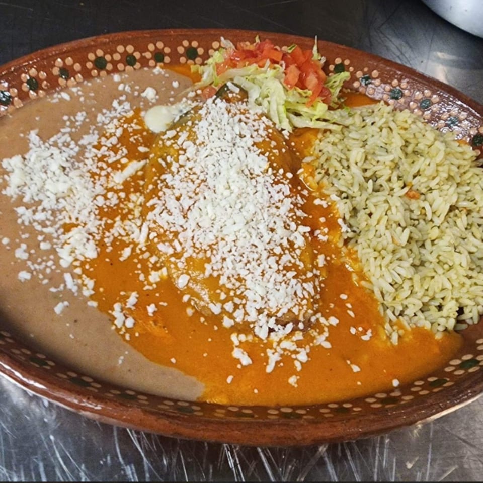 Mexican dish with enchiladas, refried beans, rice, and a side of lettuce and tomato.