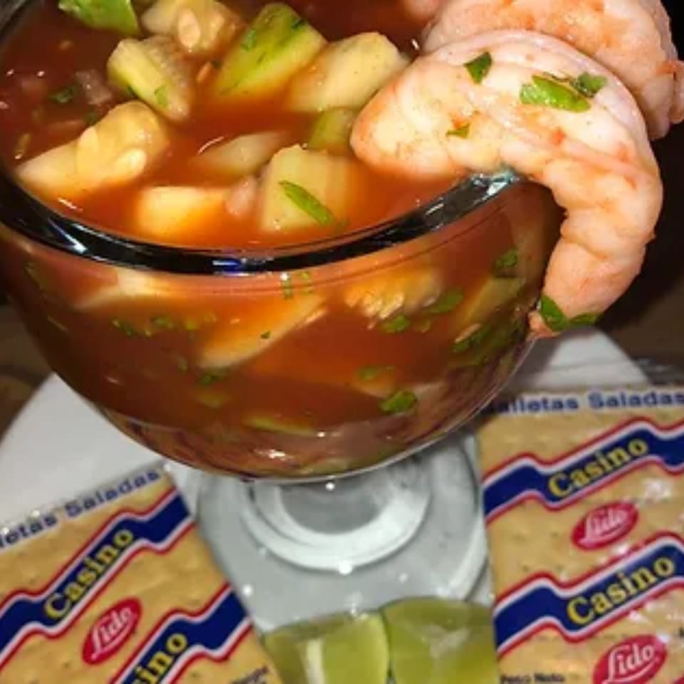 Shrimp cocktail with avocado and cilantro, served with lime wedges and crackers.